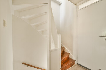 an empty room with stairs leading up to the second floor and a white door in the wall is visible on the right side