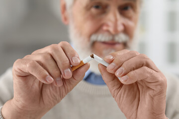 Stop smoking concept. Senior man breaking cigarette on blurred background, selective focus