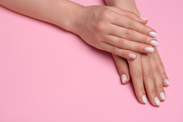 Obraz na płótnie Canvas Woman showing her manicured hands with white nail polish on pink background, closeup. Space for text