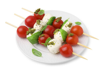 Plate of Caprese skewers with tomatoes, mozzarella balls, basil and pesto sauce isolated on white