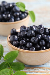 Bowls with tasty fresh bilberries and leaves on old light blue wooden table, closeup
