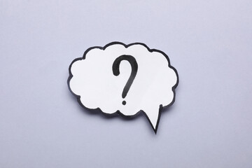 Paper speech bubble with question mark on light grey background, top view