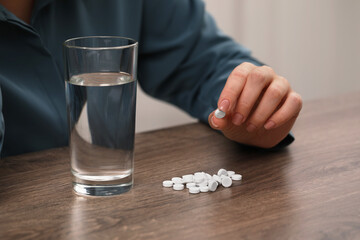 Woman with antidepressant pills and glass of water at wooden table, closeup