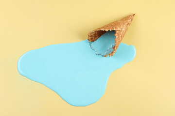 Melted ice cream and wafer cone on beige background, top view