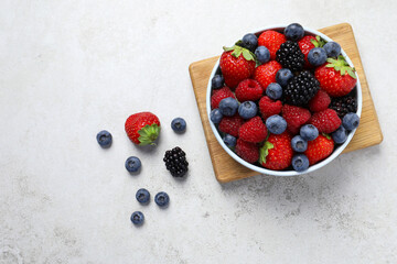 Many different fresh ripe berries in bowl on light grey table, flat lay. Space for text