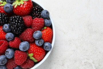 Many different fresh ripe berries in bowl on light grey table, top view. Space for text