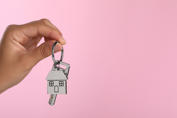 Woman holding key with metallic keychain in shape of house on pink background, closeup. Space for text