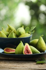 Cut and whole green figs on wooden table against blurred background, space for text