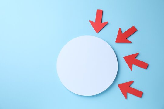 Red paper arrows and white circle on light blue background, flat lay. Space for text