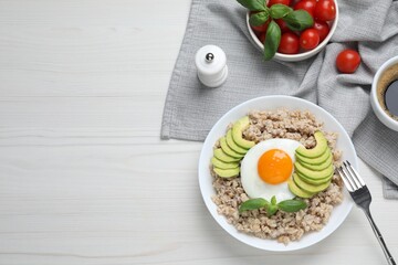 Delicious boiled oatmeal with fried egg and avocado served on white wooden table, flat lay. Space for text