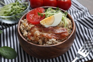 Delicious boiled oatmeal with egg, bacon and tomato on table, closeup