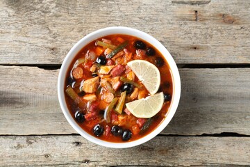 Meat solyanka soup with sausages, olives and vegetables in bowl on wooden table, top view