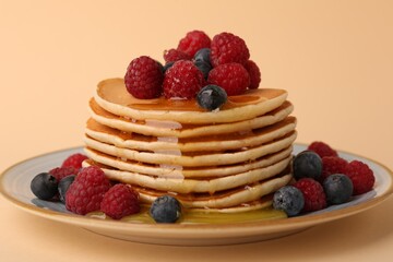 Stack of tasty pancakes with raspberries, blueberries and honey on pale orange background, closeup