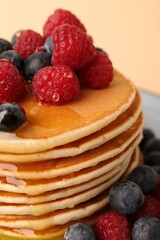 Stack of tasty pancakes with raspberries, blueberries and honey on pale orange background, closeup