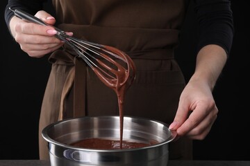 Woman with whisk mixing chocolate cream on black background, closeup