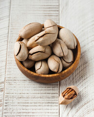 Inshell pecans in a wooden plate on a white wooden background. Nuts.