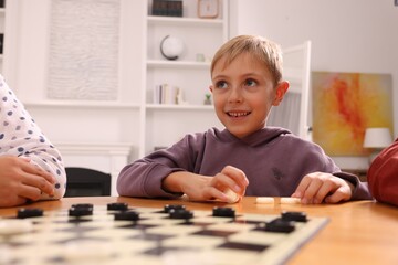 Boy playing checkers at wooden table in room