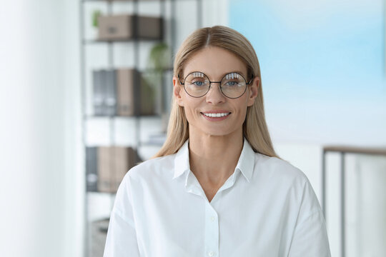 Portrait of beautiful businesswoman in glasses indoors. Confident lady with blonde hair looking into camera