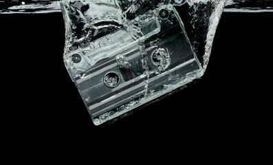 Cassette retro vintage Tape fall into clear water with air bubble. Black retro vintage cassette magnetic tape drop to wash old time. Black background isolated freeze element