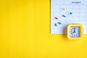 Calendar with colorful pins and clock, top view. On yellow background, copy space.