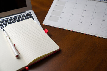 Notepad on top of laptop and next to calendar or planner. On top of wood table. Copy space.