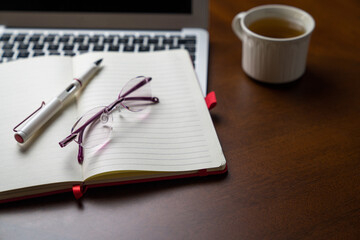 Eyeglasses on top of notepad and computer laptop and next to a cup of tea. Copy space.