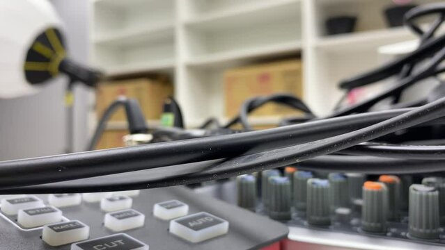 Audio equipment mixer console controller, video capture switcher and black wire cable on table inside studio close up view. 