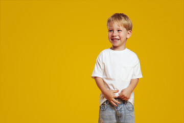 Excited shy blonde child wearing white casual t-shirt smiling and looking at free empty space for...