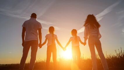 Sun rays fall on family silhouettes holding hands in field with plants at sunset. Concept of relationships and spending time in nature in evening, sunlight - obrazy, fototapety, plakaty