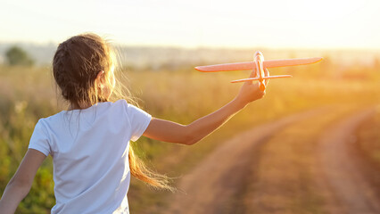 Female child runs along paved road of plain playing with toy plane. Fun time concept and flight...
