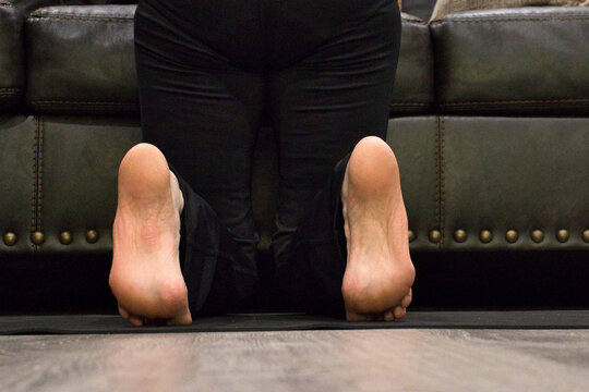 Woman stretching feet on a black yoga mat in a living room.