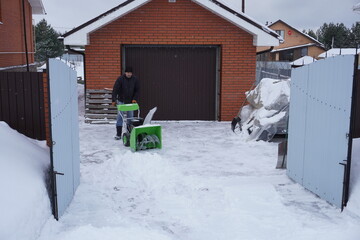 A man cleans snow in the winter in the courtyard of the house,  man cleaning snow with a snow blower