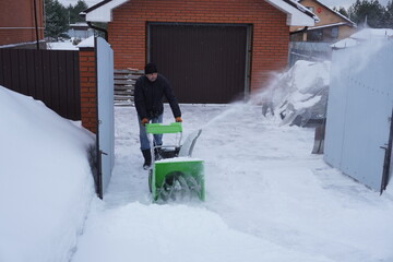 A man cleans snow in the winter in the courtyard of the house,  man cleaning snow with a snow blower