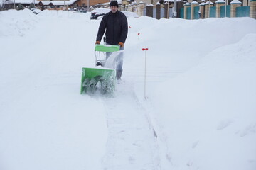 A man cleans snow in the winter in the courtyard of the house,  man cleaning snow with a snow blower