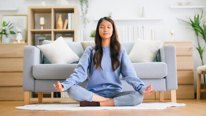 Happy young Asian woman practicing yoga and meditation at home sitting on floor in living room in...