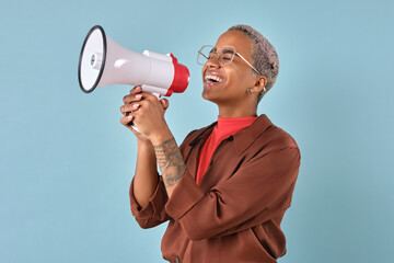 Young laughing attractive African American millennial woman in glasses holds megaphone in hands to...
