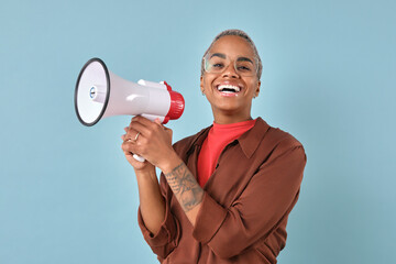 Young cheerful attractive African American woman holds megaphone with both hands and looks at...