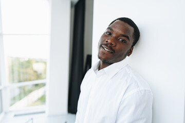 Young african man in white shirt and glasses posing near large window