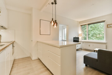 a kitchen and living room in an apartment with white cabinets, wood flooring and large windows overlooking the trees