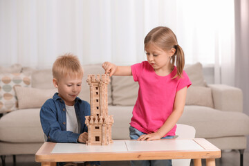 Little girl and boy playing with wooden tower at table indoors. Children's toy
