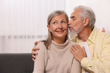 Senior man kissing his beloved woman at home, space for text