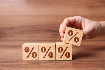 Woman arranging cubes with percent signs on wooden background, closeup. Space for text