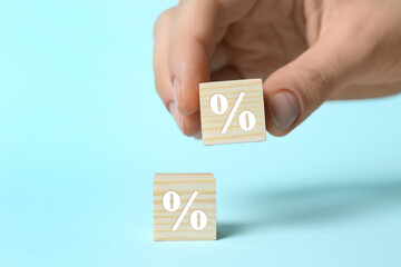 Woman arranging cubes with percent signs on light blue background, closeup
