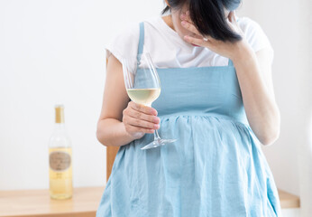 Pregnant woman wearing a blue dress holds wine glass and has headache
