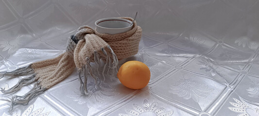 Cup with a teaspoon wrapped in a scarf and lemon on a white background
