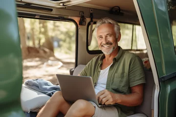 Foto op Plexiglas Happy older man sitting in rv camper van using laptop. Smiling mature active traveller holding computer on lap remote working online and enjoying freedom, resting in outdoor camping © sam
