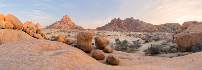 Panoramic, desert landscape of famous rounded red, granite rocks of Spitzkoppe area in early sunrise against blue sky. Picturesque rocky desert photo in calm morning in Spitzkoppe, Namibia.