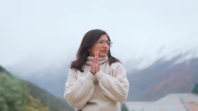 Portrait of Indian teenager girl rubbing hands during cold winter day in Himachal Pradesh, India. Girl wearing warm clothes and standing against snowy Himalayan mountains.