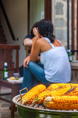 Primo piano di grigliata di mais in giardino con ragazza di spalle sullo sfondo