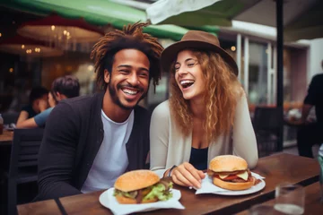 Tuinposter multiracial couple of a redhead girl and an african american boy laughing eating a hamburger © Alvaro